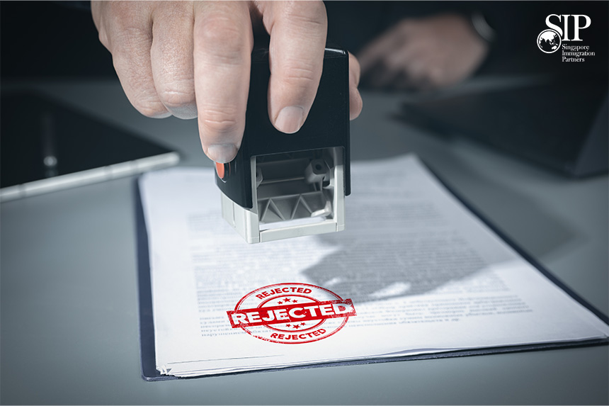 Close-up of a hand stamping a document with a red “REJECTED” mark in an office setting.